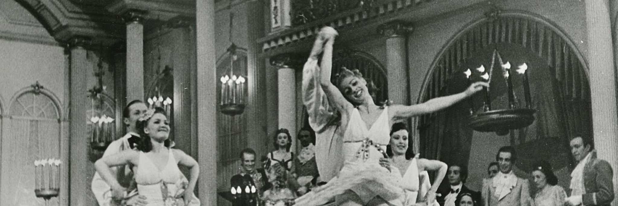 Bilde av teaterforestilling med en rekke aktører. Noen av dem danser, andre ser på i bakgrunnen