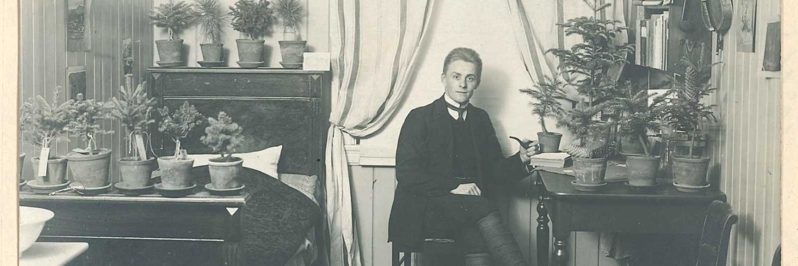 ørund Midttun (1887-1969) på Norges Landbrukshøgskole i Ås i 1911. Rommet er fullt av småtrær, og fela henger på veggen. Fotografiet er hentet fra den minneboken som dekker 1910-1911.