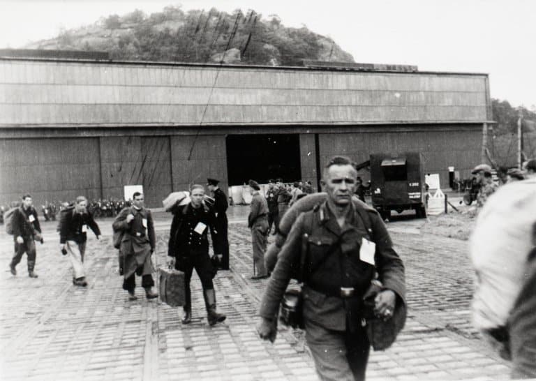 Tysk personell ved flyhangaren på Vestnes som trolig er blitt plukket ut for ytterligere forhør før repatriering (forflytning og hjemsendelse) til Tyskland etter frigjøringen i 1945. Hangaren på Vestnes i Mandal hvor tyske styrker fra Rogaland, Vest- og Aust-Agder ble samlet, fungerte som en gjennomgangsstasjon og -leir før repatriering. Fotograf er trolig Alf Endsjø, politifotograf i Stavanger politidistrikt (fra arkivet etter Christian Benneche/Arkivverket/Statsarkivet i Stavanger).