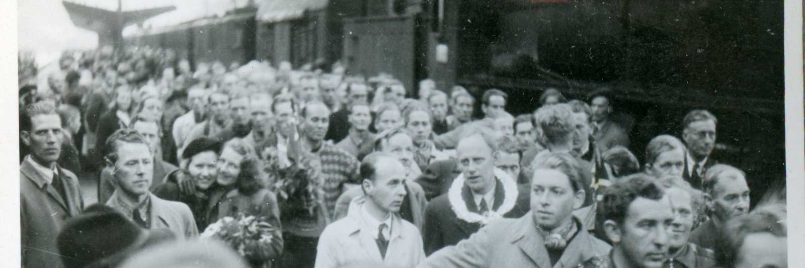 "Tysklandsfanger kommer" (original bildetekst). Foto fra album etter Leon Jacobsen. Den 28. mai 1945 skrev Bergens Tidende dette om begivenheten som fant sted samme dag: "Den lykkeligste dag i vårt liv... Studenter, brannmenn, Telavågfolk og andre fanger hjem fra Tyskland i dag. En gripende mottagelse ved jernbanestasjonen hvor tusener av mennesker var samlet".