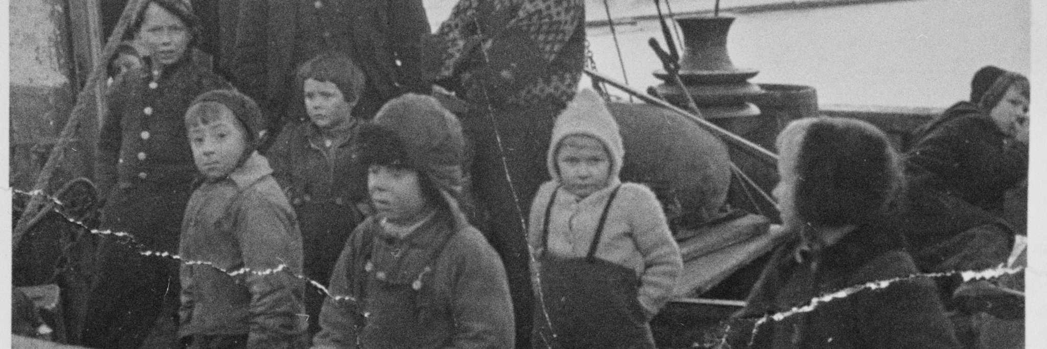 Utsnitt av fotografi fra Finnmark under 2. verdenskrig. Sivilbefolkningen ble evakuert og på bildet sees barn som blir fraktet i småbåter over til det ventede britiske krigsskipet. Foto: ukjent, utlån: NTBs krigsarkiv/Digitalarkivet.