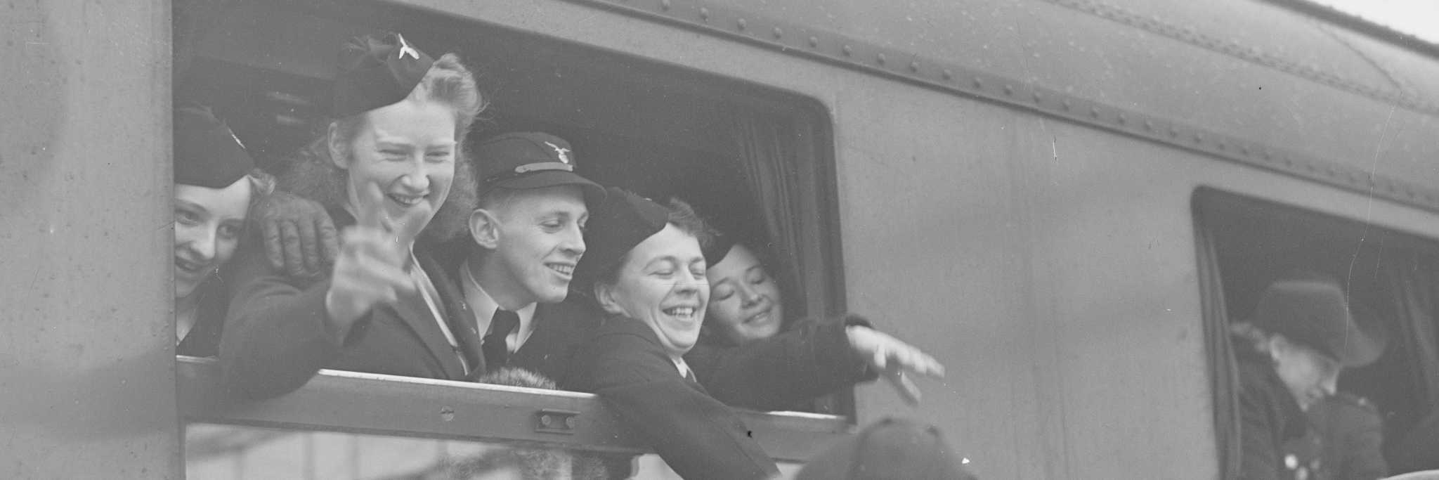 Bildet viser en gruppe unge mennesker fra Nasjonal Samlings Ungdomsfylking som vinker ut av togvindu- Unghirdens avreise til Garmisch 18. februar 1941
