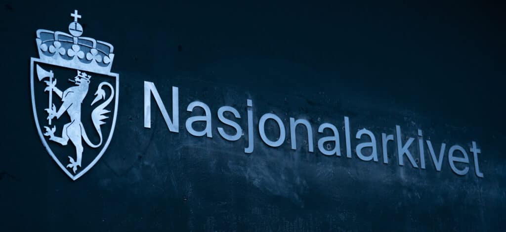 Skilt for Nasjonalarkivet med norsk våpenskjold på mørk bakgrunn, opplyst hvit skrift.