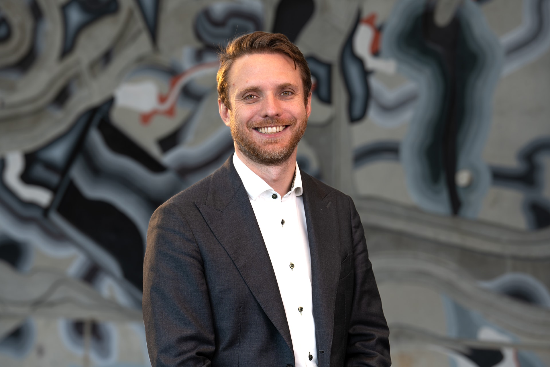 Smilende mann foran betongvegg med abstrakt kunst