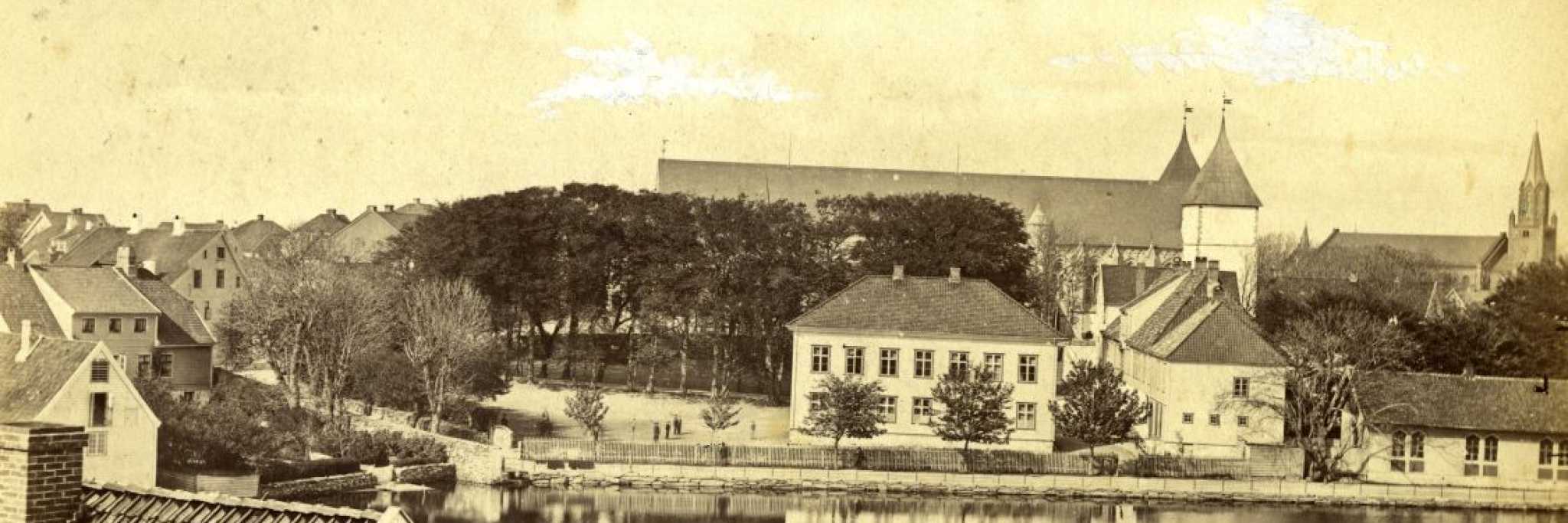 Historisk fotografi av området rundt Kongsgård skole i Stavanger. Til høyre står tre skolebygninger, inkludert den lave gymnastikksalen fra 1862. Bak sees St. Petri kirke og Stavanger domkirke. Til venstre ligger Alexander Kiellands barndomshjem, med byfogd Christensens hus bak og Gunder Thorsens garveri i forgrunnen. Bildet er tatt mellom 1866 og 1900. Fotograf ukjent.