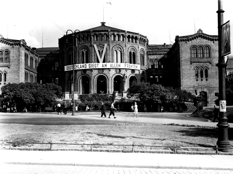 Sort hvitt bilde fra 1940. Tyskerne har på Stortingets fasade hengt opp en Stor V og et banner som sier Deutschland siegt an allen fronten. Tyskland seirer på alle fronter.