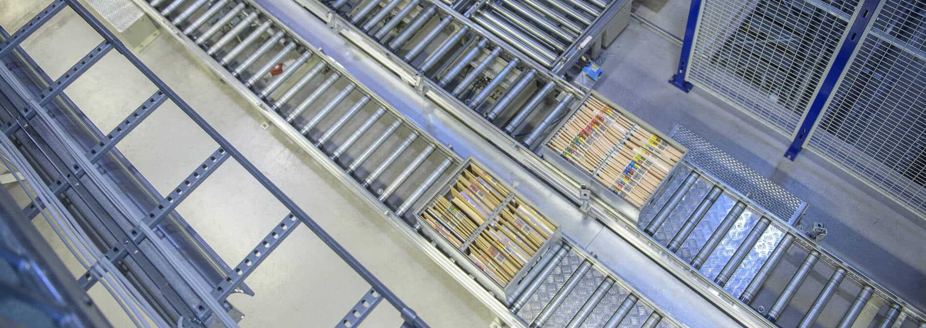 Luftfoto av industrielt transportbåndsystem med rulleskinner, metallrister og blå støttestrukturer i et lagermiljø.