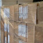 Stablede pappesker pakket inn i plast, merket med fraktetiketter og QR-koder, klare til distribusjon eller lagring.
