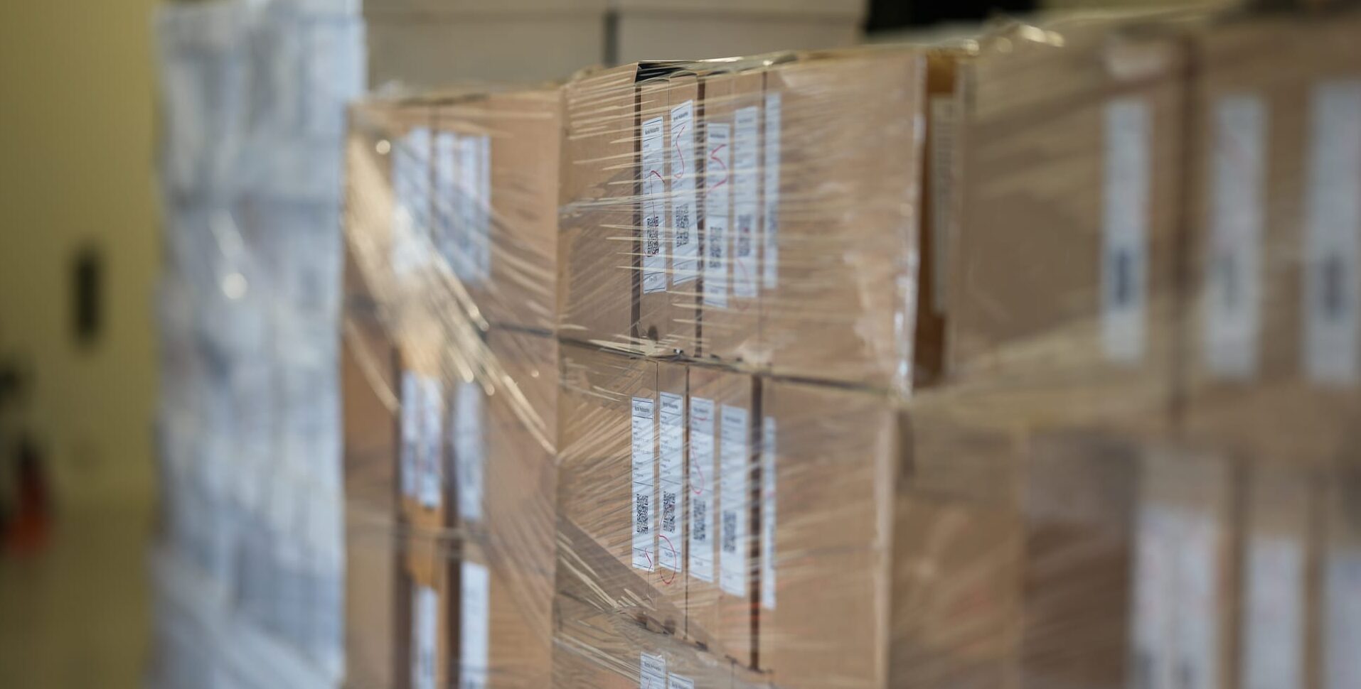 Stablede pappesker pakket inn i plast, merket med fraktetiketter og QR-koder, klare til distribusjon eller lagring.