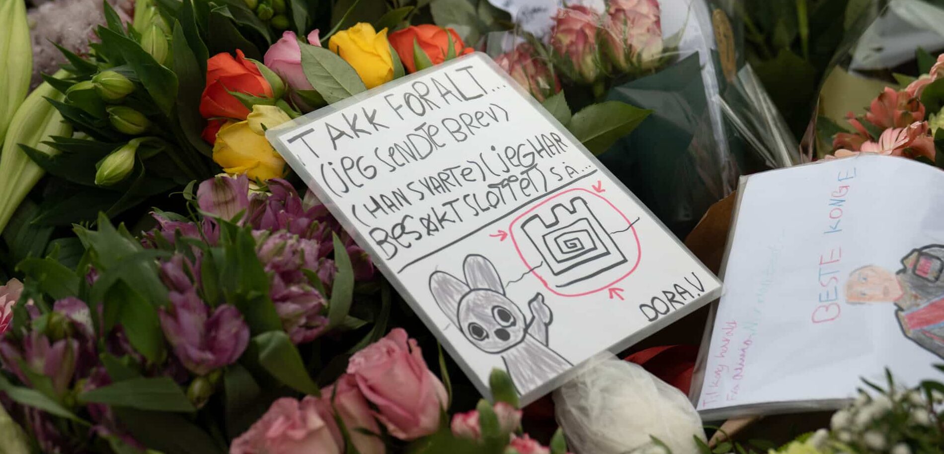 Nærbilde av blomster og hilsener. En håndtegnet hilsen ligger blant blomstene.